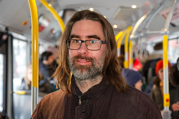 A man in a beard standing in a city bus