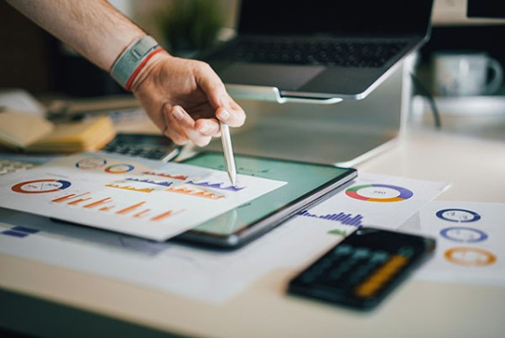 A person points at a tablet. There are papers around it with graphs.