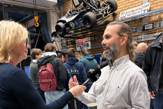 A man interviewed by a woman with students in the background