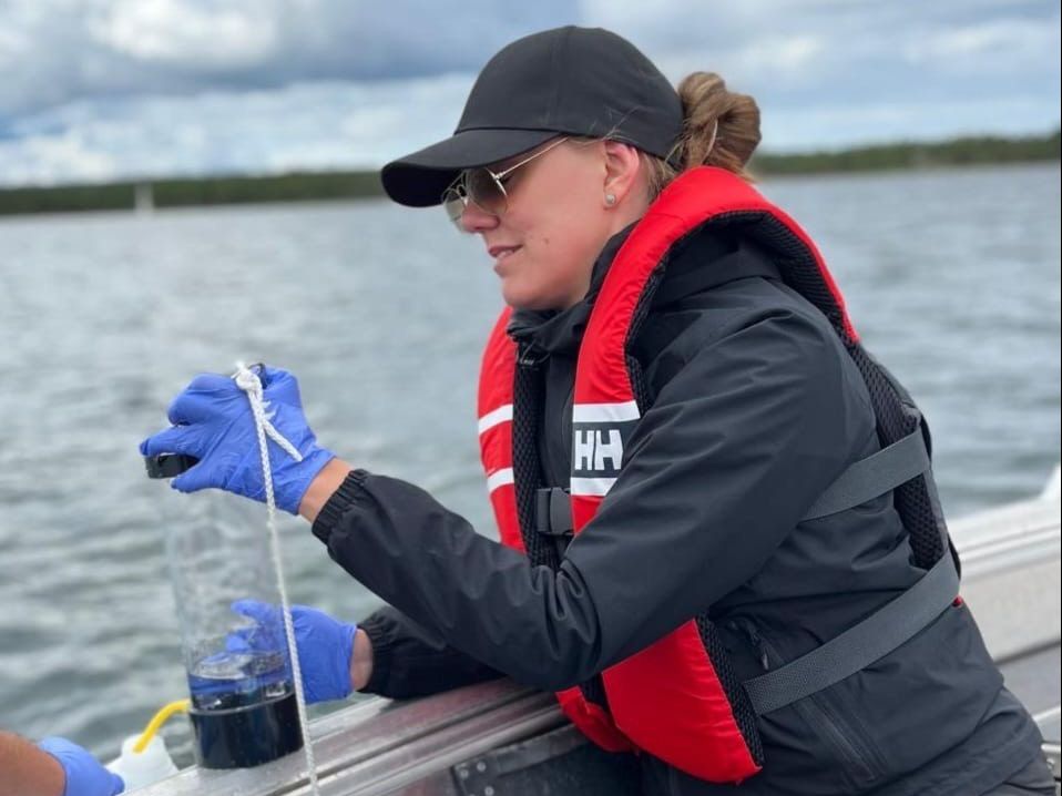En kvinna i en båt tar vattenprov